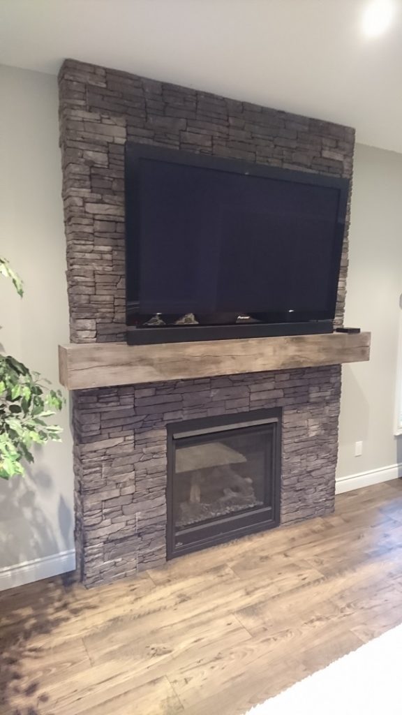 Gas fireplace with TV mounted above beam. Stone veneer is Farmledge Westchester by Stonecraft.